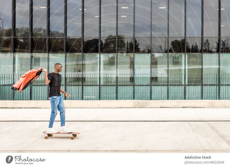 Cool young black man riding skateboard on modern city street ride building trendy cool skater activity style confident millennial male african american ethnic