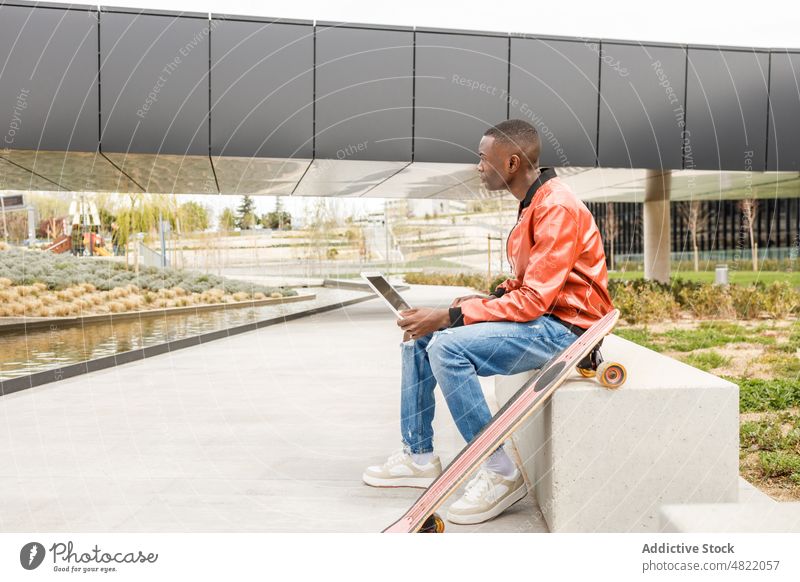 Young black guy using netbook on bench in park man work laptop freelance remote typing concentrate longboard busy city male young african american ethnic trendy