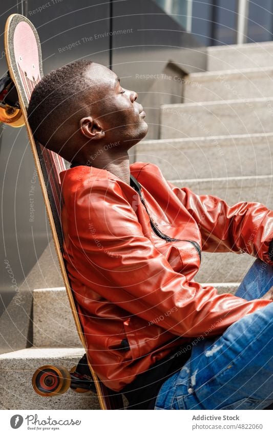 Tranquil African American guy leaning on skateboard on street stairs man eyes closed relax staircase trendy cool skater free time rest student generation z male