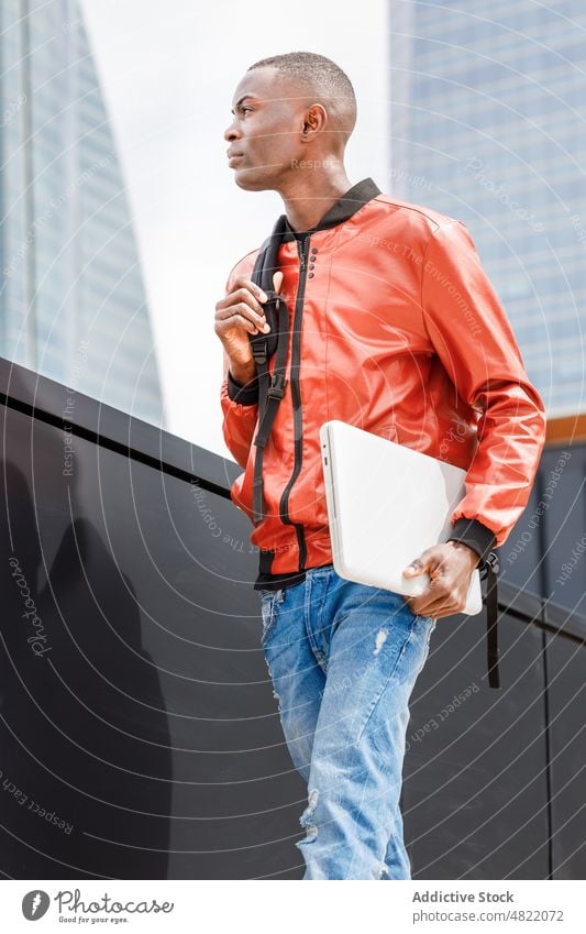 Confident black male student strolling near modern building in city man walk street backpack laptop confident serious trendy urban generation z contemporary