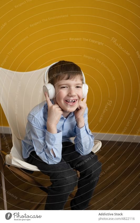 Boy listening to music on deckchair boy home smile happy meloman entertain kid smart casual sit gesticulate cheerful headphones wireless child song sound bright