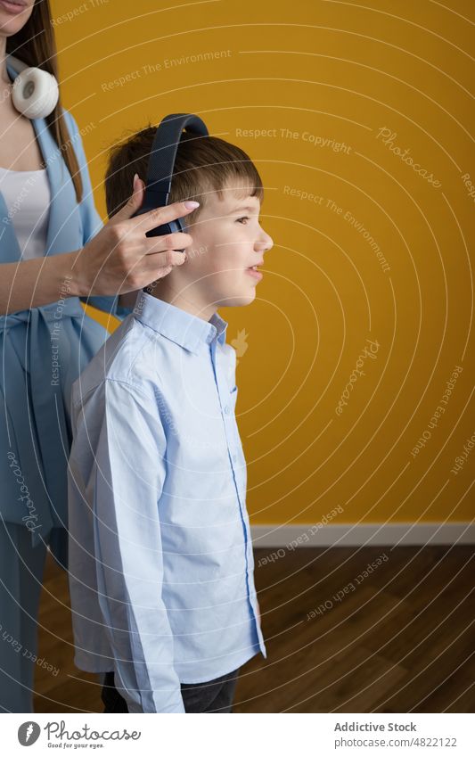 Mom putting headphones on son mother adjust music listen put on together home woman boy meloman wireless child kid tune parent smile love mom entertain positive