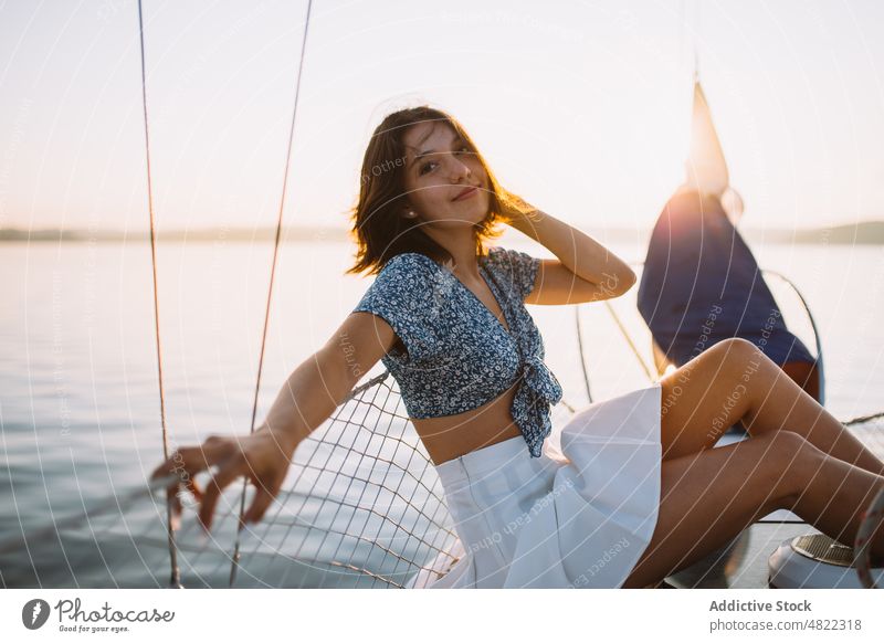 Stylish female tourist resting on yacht and looking at camera woman admire sea sailboat traveler sunset vacation cruise holiday style portrait trendy trip young