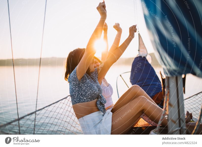 Happy ladies chatting during cruise on sea at sunset women sailboat friend raised arms summer vacation together yacht happy smile talk relax trendy young