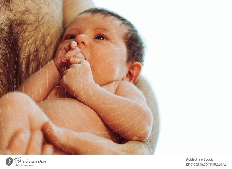 Cute infant sucking hand while being hold by dad in white studio baby man father love newborn hug fatherhood tender innocent finger adorable male shirtless