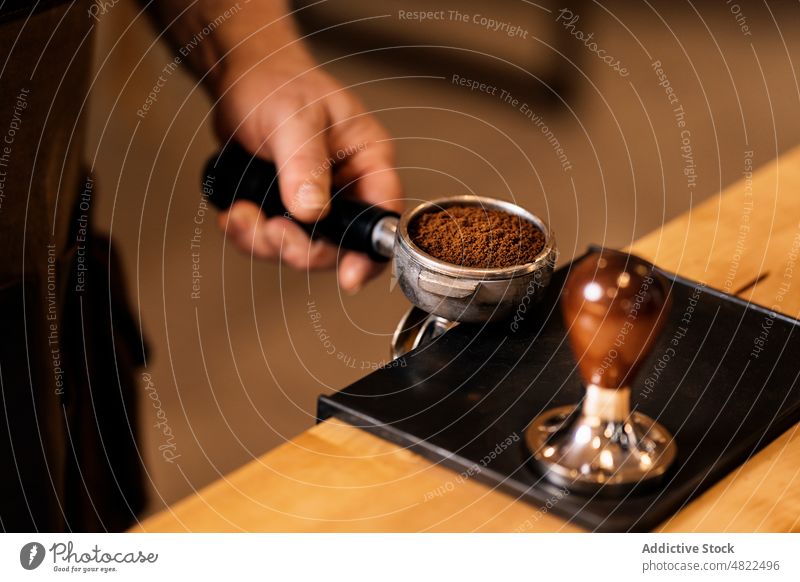 Crop anonymous man using tamper for pressing ground coffee in portafilter espresso barista cafe coffee shop prepare beverage coffee house male hand professional