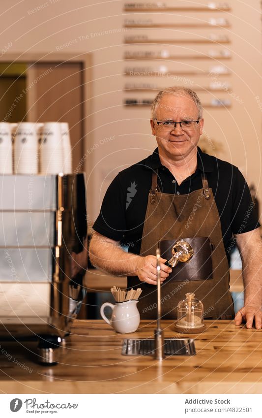 Senior barista with portafilter in hand smiling in coffee house man coffeemaker smile positive counter cafe portrait coffee shop work small business employee