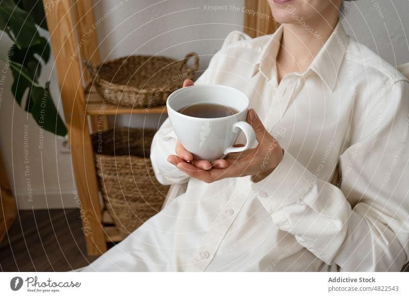 Anonymous lady sitting on chair and drinking coffee in morning woman rest home happy plant apartment beverage enjoy recreation female young casual dark hair