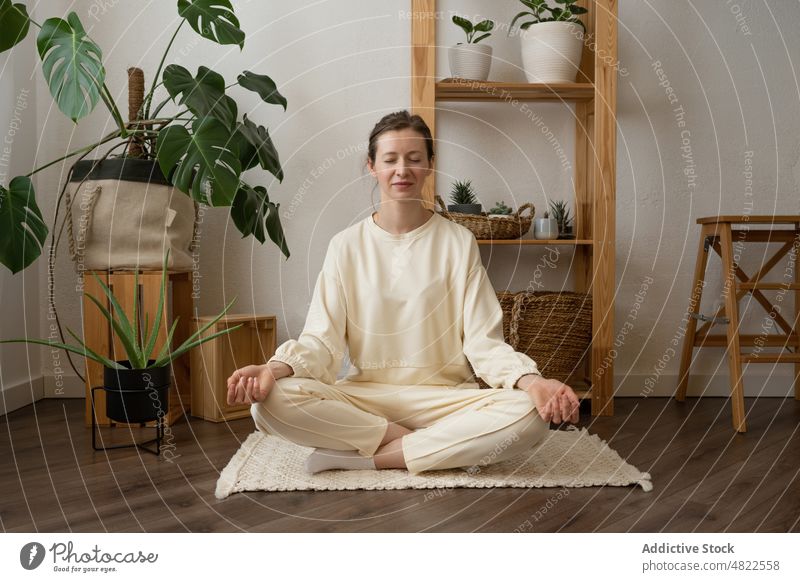 Peaceful woman meditating in Lotus yoga pose at home lotus pose padmasana meditate eyes closed zen stress relief practice wellness calm female young mindfulness
