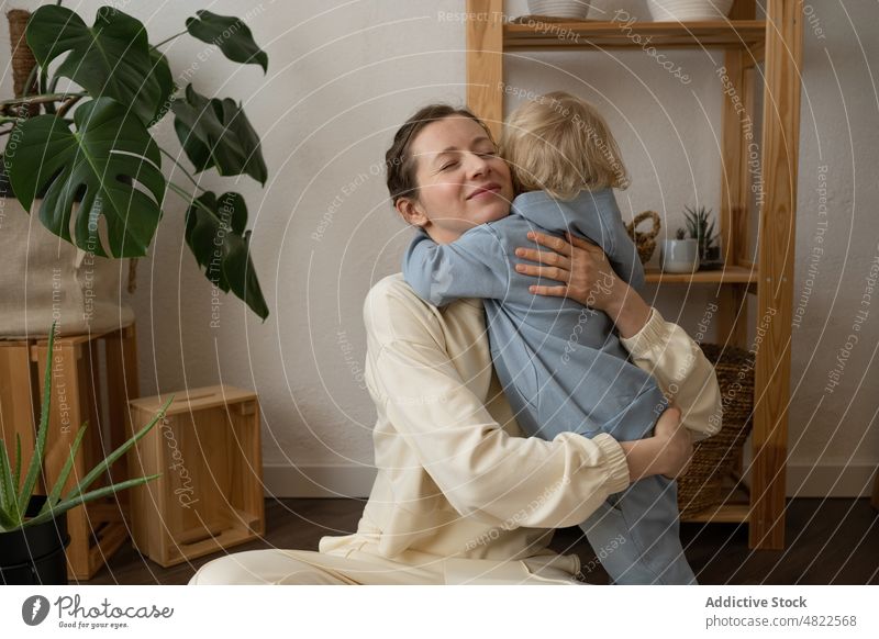 Content mom sitting on floor and hugging child at home woman embrace love legs crossed happy mother motherhood positive apartment eyes closed adorable together