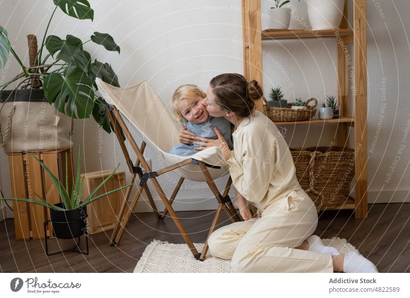 Content mom sitting on floor and hugging child at home woman kiss chair love happy mother motherhood embrace positive apartment adorable together female young