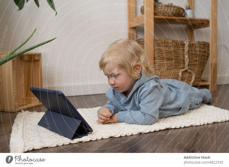Cute toddler lying on floor and watching video on tablet child curious interest attentive cartoon internet interesting apartment casual blond childhood online