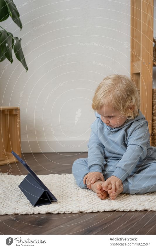 Cute toddler sitting on floor and watching video on tablet child curious interest attentive cartoon internet interesting apartment casual blond childhood online