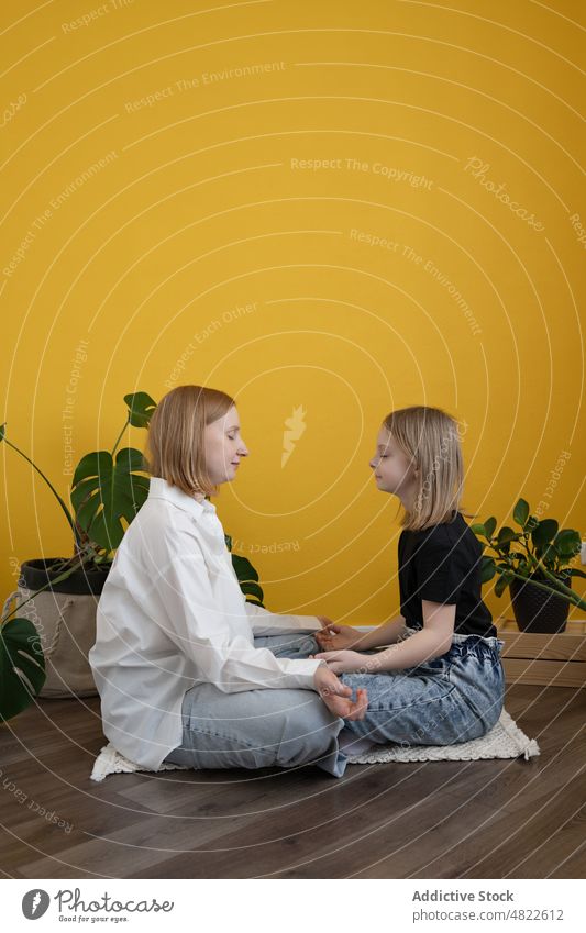 Calm mother and daughter meditating in Padmasana pose with closed eyes woman child lotus pose padmasana meditate yoga eyes closed together zen wellbeing