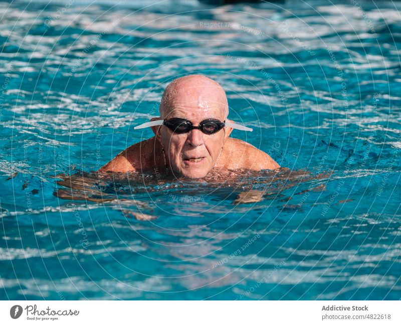 Senior man in goggles swimming in pool on sunny day holiday active vacation summer elderly senior portrait healthy practice leisure activity water male bald