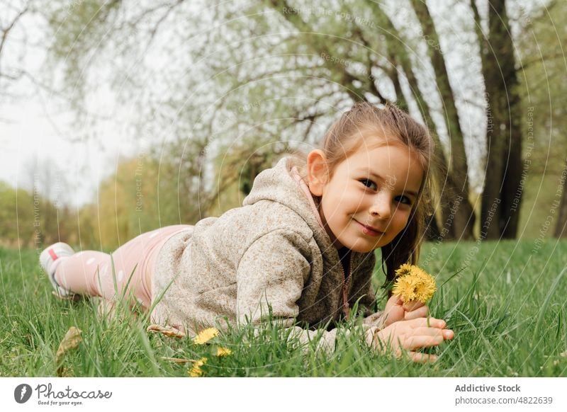 Positive little kid lying on meadow with bunch of dandelions in park girl lawn smile happy child flower pick relax grass positive long hair warm clothes nature