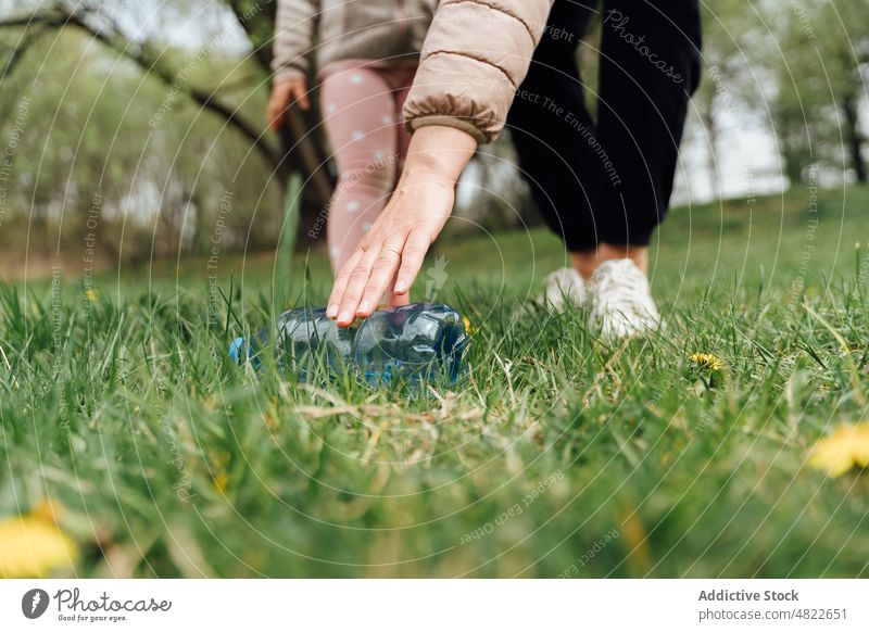 Crop faceless female with kid picking up bottle from grassy meadow woman child pick up ecology nature forest mother daughter garbage park spend time ecosystem