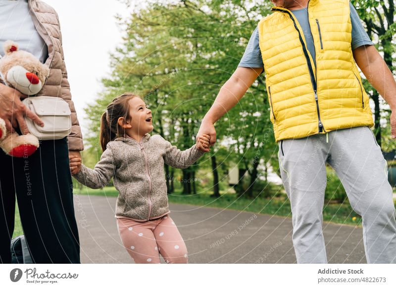 Cheerful little kid holding hands of grandparents in park child walk happy spend time together granddaughter relationship cheerful joy raise girl casual mature