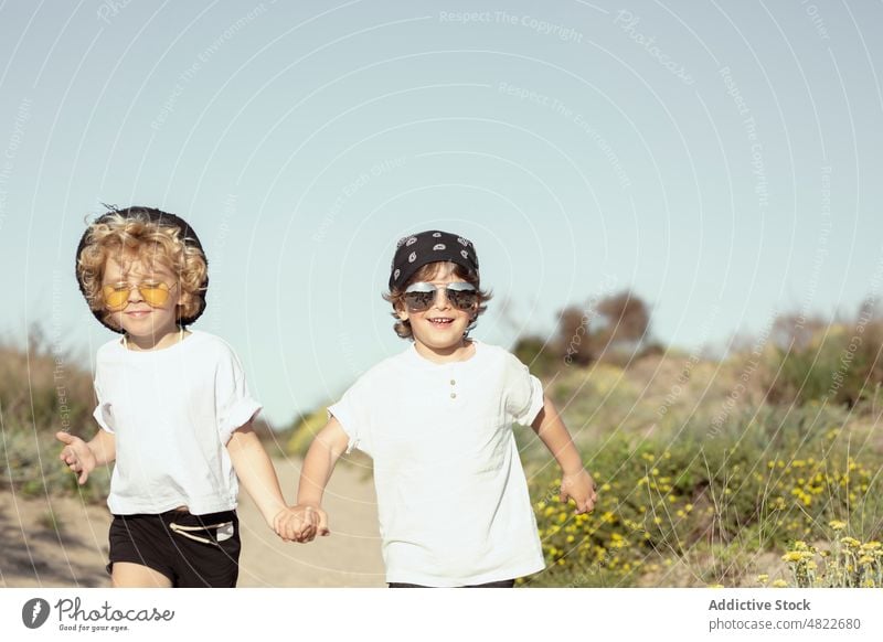 Happy little siblings holding hands while strolling on beach children walk path together happy trendy brother holiday plant cheerful kid toddler blond style