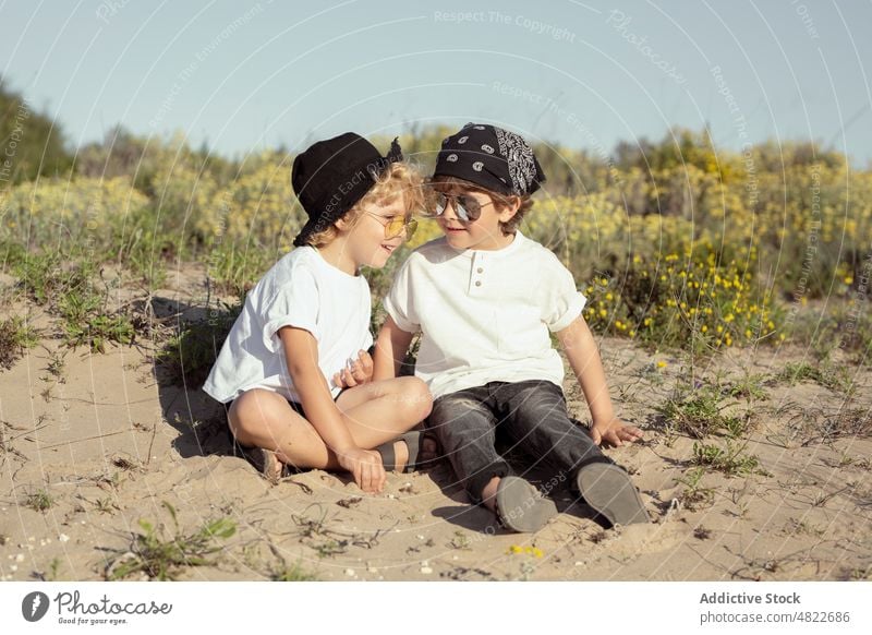 Adorable positive kids playing with sand on beach children holiday cheerful together back to back smile vacation brother joy friendship happy trendy blond style