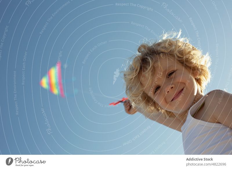 Cheerful child smiling and camera while launching colorful kite smile excited summer happy childhood vacation boy blue sky cloudless cheerful joy kid blond