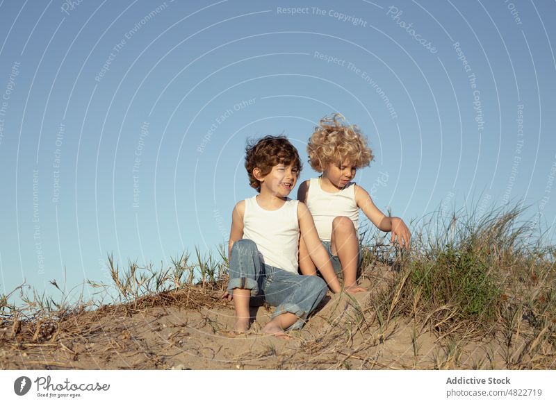 Adorable positive kids playing with sand on beach children holiday cheerful together smile vacation brother joy friendship happy trendy blond style coast