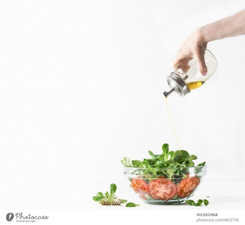 Woman hand pouring  oil over big bowl with salad. Healthy food. woman making fresh green lettuce tomatoes olive oil white background healthy food vegan above