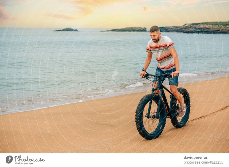 Man riding a fat bike on the beach young man copy space person sport bicycle wheel tracks lifestyle sea scenery wheel marks active bicyclist biking male guy