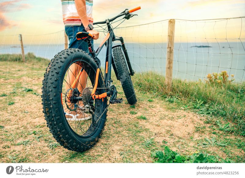 Fat bike on the beach with guy holding it fat bike coast unrecognizable sea person sport copy space standing bicycle lifestyle scenery fence active bicyclist