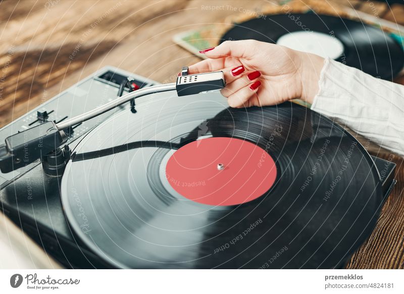 Young woman listening to music from vinyl record player. Playing music on turntable player. Female enjoying music from old record collection at home analog