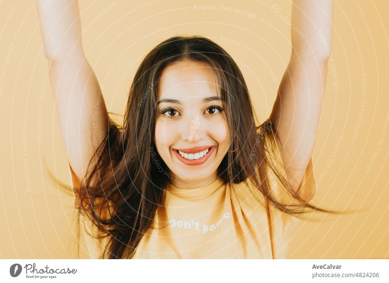 Young brunette girl over isolated yellow background celebrating and having fun waving hands and hair. Happy woman. People sincere emotions lifestyle concept