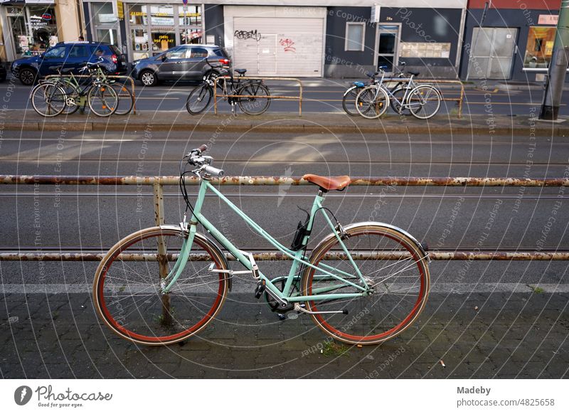 Classic ladies bike in turquoise on a rusty railing at a streetcar stop in the summer in the district of Sachsenhausen in Frankfurt am Main in Hesse Sidewalk