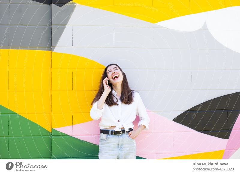 Young woman holding a mobile phone and video chatting standing near vibrant colorful wall in the city. Happy woman smiling and using technology. beautiful