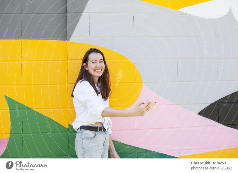 Young woman holding a mobile phone and video chatting standing near vibrant colorful wall in the city. Happy woman smiling and using technology. beautiful