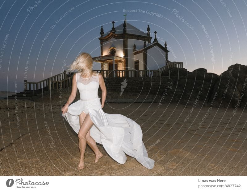 What a romantic way to get married on a beach in Porto, Portugal. A small church is by the ocean, the skies are purple on this fine evening, and a gorgeous blonde bride is dressed in a white wedding dress. No groom on the image though.