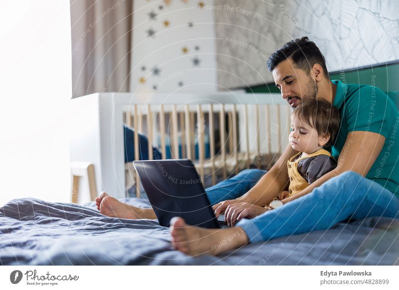 Young man and his son using a laptop at home adult affection baby bonding boy candid care child childhood domestic enjoying family fun happiness happy house