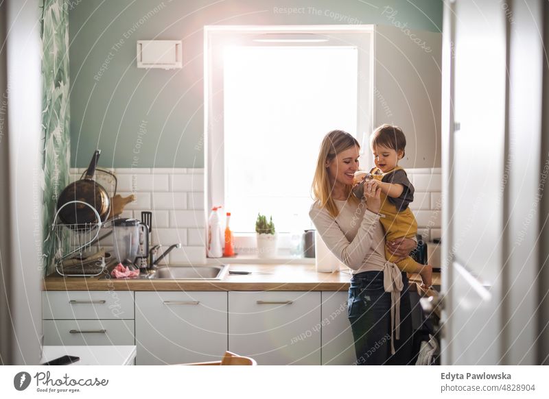 Young mother with child in the kitchen adult affection baby bonding boy candid care childhood domestic enjoying family fun happiness happy home house indoors