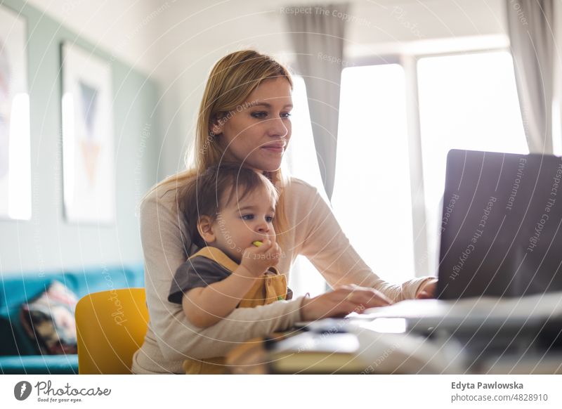 Mother working on laptop with child sitting on her lap adult affection baby bonding boy candid care childhood domestic enjoying family fun happiness happy home