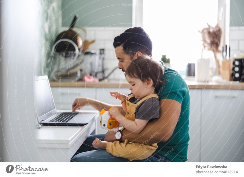 Dad working on laptop with child sitting on his lap adult affection baby bonding boy candid care childhood domestic enjoying family fun happiness happy home