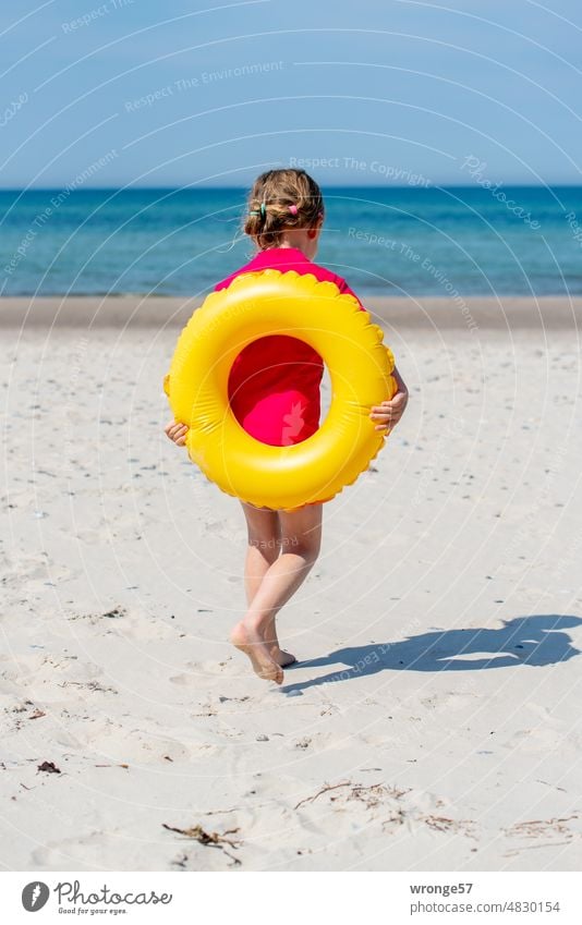 Girl running towards the sea on the beach of the Baltic Sea with a yellow swimming ring on her back Baltic beach swim ring Floating tyres Ocean Walking