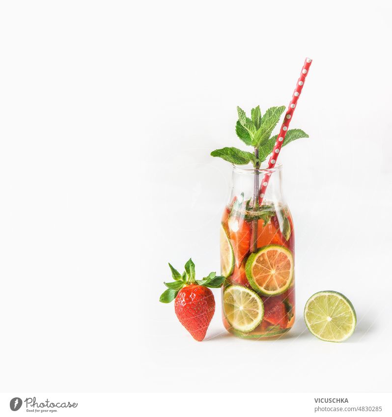 Lemonade in bottle with drinking straw and ingredients: strawberry and lime slice at white background. lemonade summer refreshing drink fruits healthy lifestyle