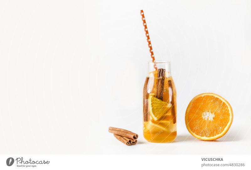 Tasty lemonade in bottle with drinking straw and ingredients: orange and cinnamon sticks at white background. tasty summer refreshing fruits healthy lifestyle