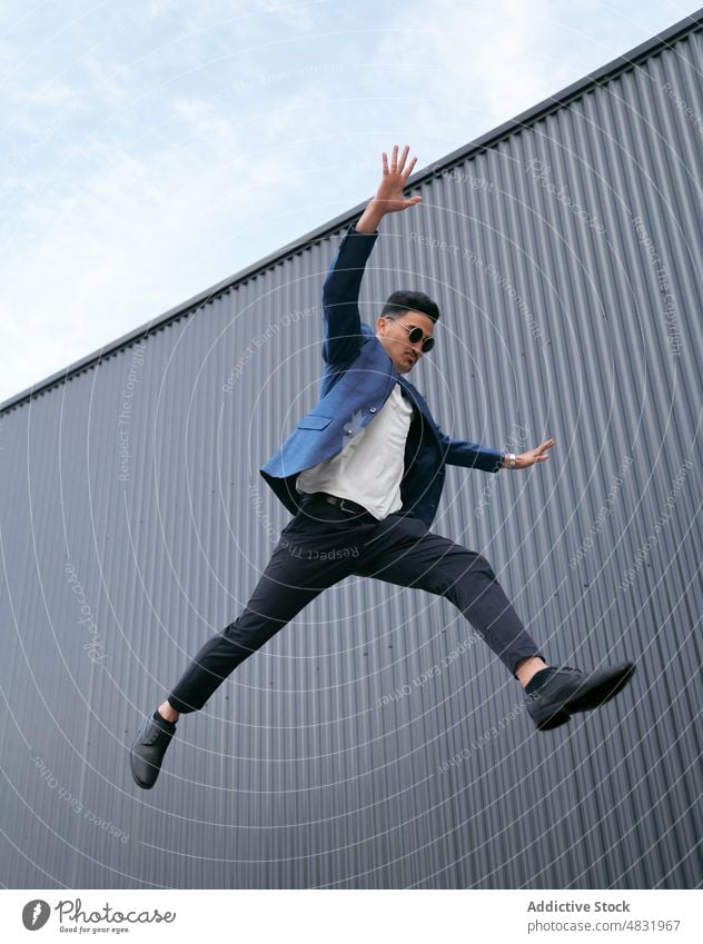 Male entrepreneur jumping against metal wall businessman leap street urban concept style energy suit spread arms male daytime ethnic manager modern sunglasses