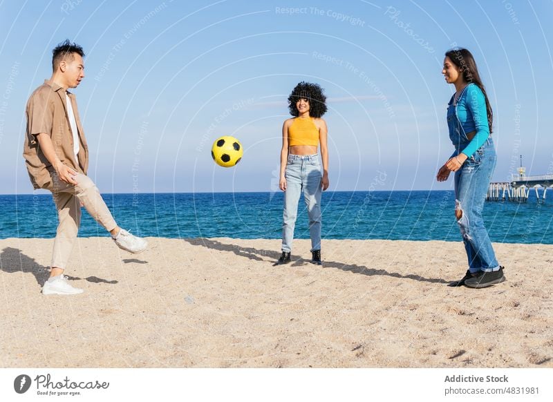 Diverse man and woman playing with ball on beach friend kick summer weekend together sea resort blue sky vacation shore coast happy sand friendship seaside