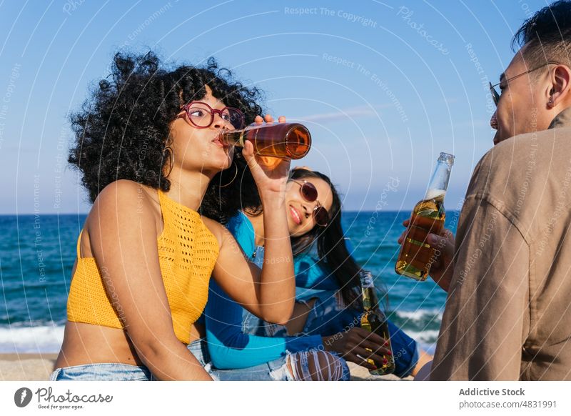 Black woman drinking beer with friends beach sea bottle together weekend summer rest women diverse multiracial multiethnic black african american hispanic asian