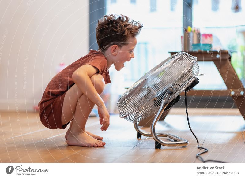Little boy at home sitting on the floor playing with fan blow game young enjoying blowing expression fun mouth open motion male happy apartment room electric