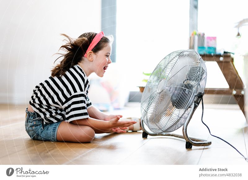 Little girl at home sitting on the floor playing with fan blow game young enjoying blowing expression fun motion female happy apartment room electric childhood