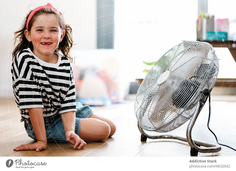 Little girl at home sitting on the floor playing with fan blow game young enjoying blowing expression fun motion female happy apartment room electric childhood