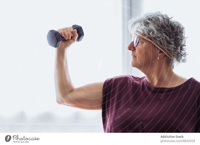 Strong elderly woman exercising with dumbbell exercise bicep training fitness morning home strong weight female aged senior pensioner retire wellness workout