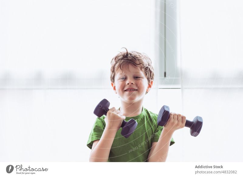 Cheerful boy exercising with dumbbells exercise training fitness smile home morning happy gymnastic kid window child healthy lifestyle activewear vitality